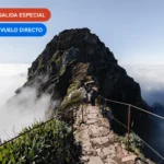 Sendero de montaña entre cumbres rocosas y un mar de nubes en Madeira, Portugal.